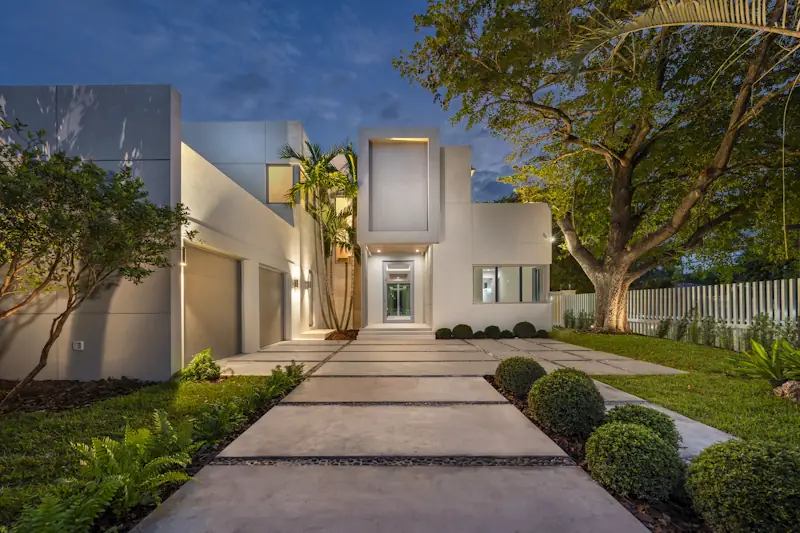 White modern home with flat roofs and a lit front walk at dusk